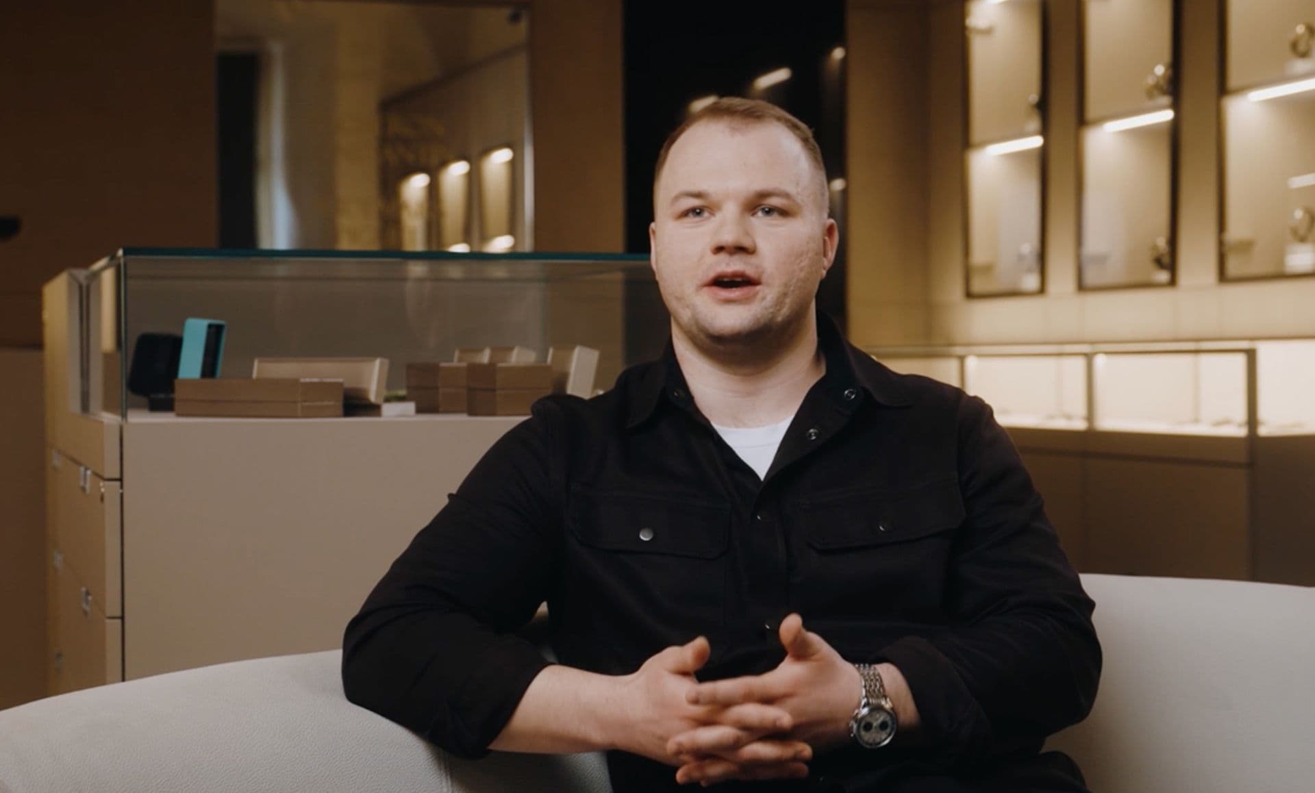 man wearing a dark shirt sat on a white couch in a luxurious showroom