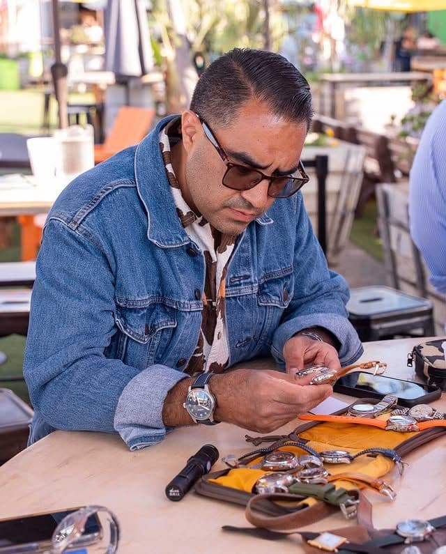 man in denim jacket and sunglasses looking intently at a watch in his hand