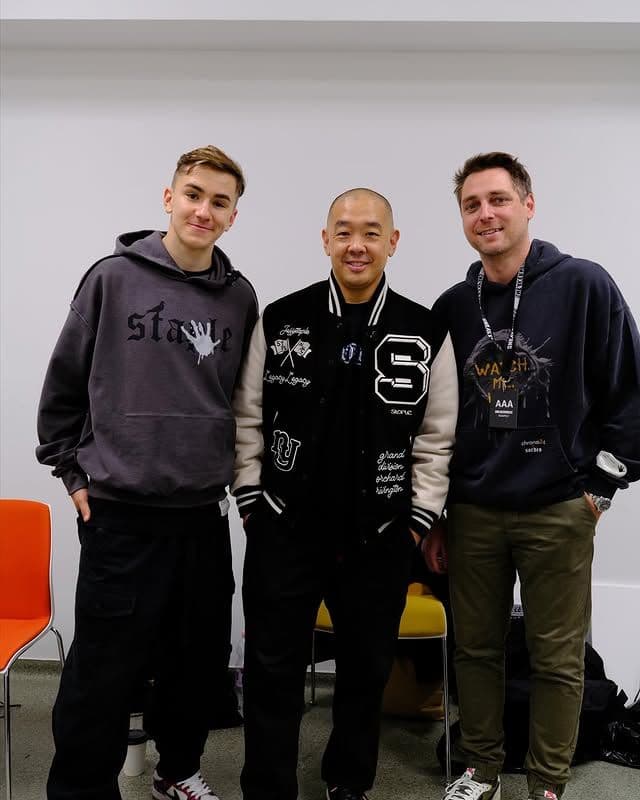 three men posing in front of a white wall wearing street style clothing