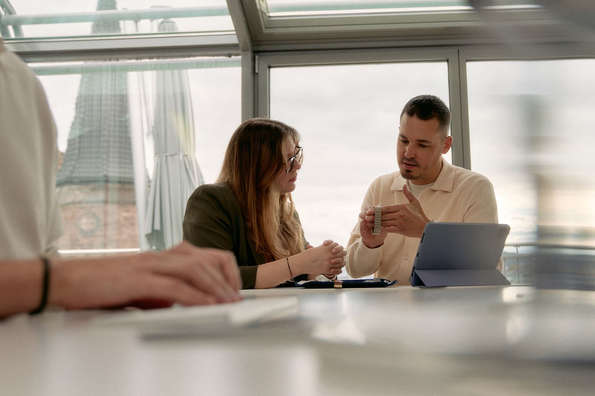 man and woman sat in a brightly lit glass room with a touchpad and examining a watch