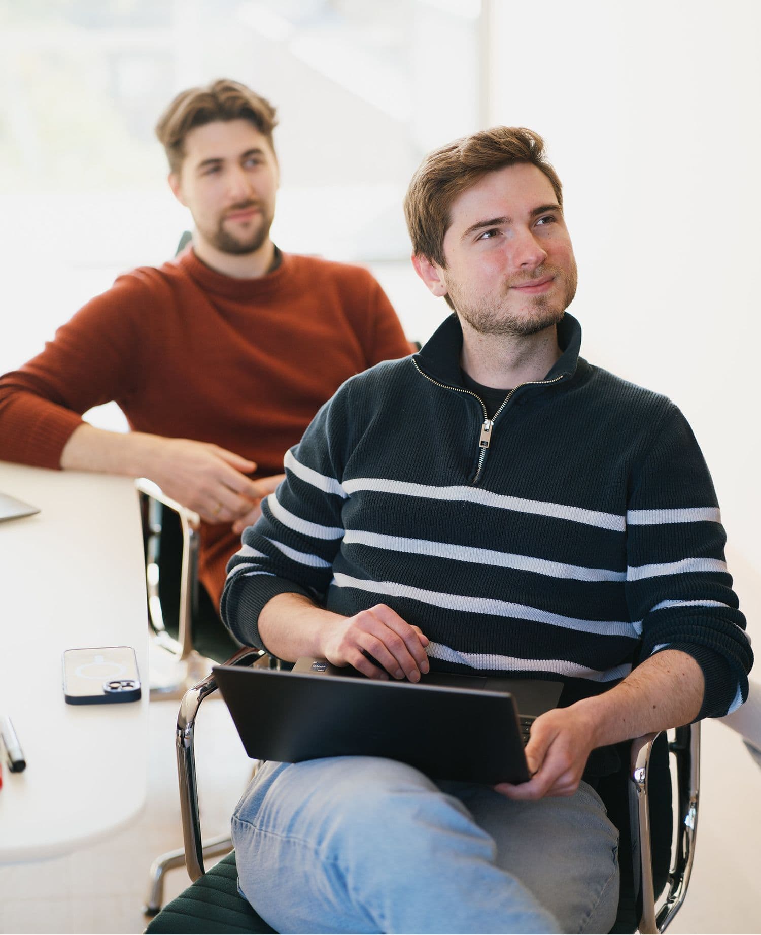 Zwei Personen sitzen in einem hellen Besprechungsraum, eine hält ein Laptop.
