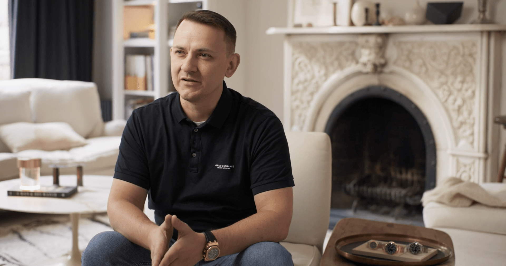 man in black polo shirt sat in light room with fireplace