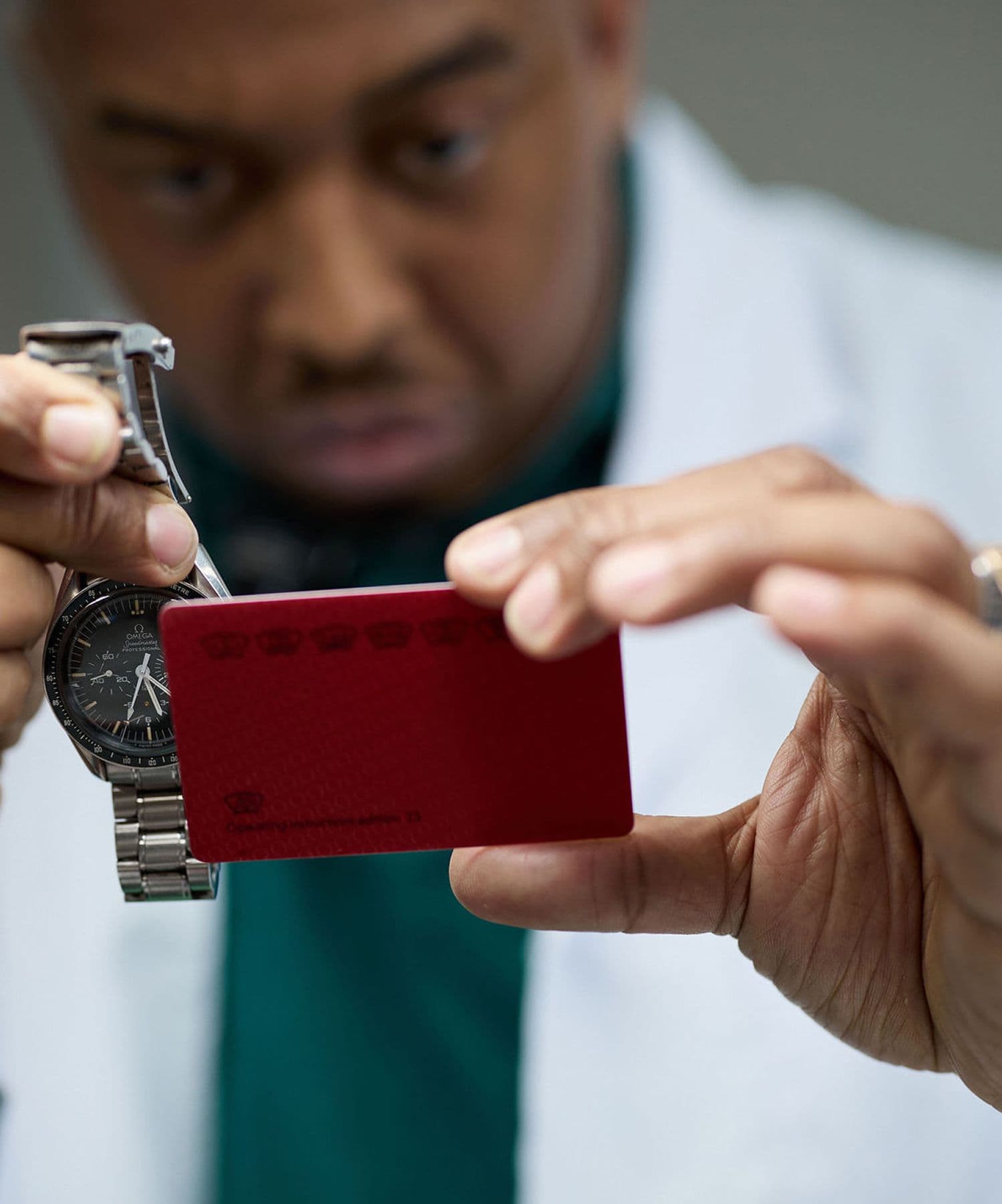 man wearing a green shirt and white coat holding up a watch and red card