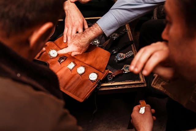 leather watch display showing a number of luxury watches while people point to them