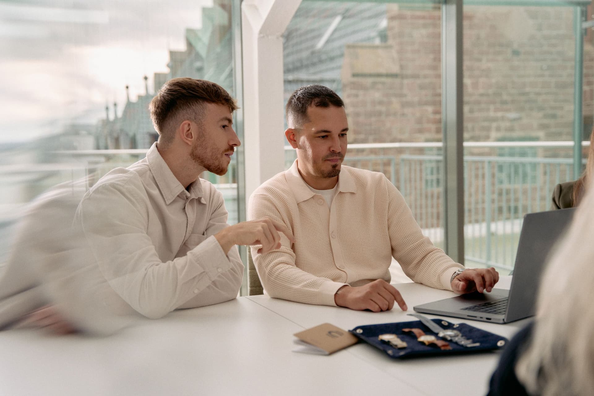 two men wearing light-coloured shirts sat at a computer with watches in front of them