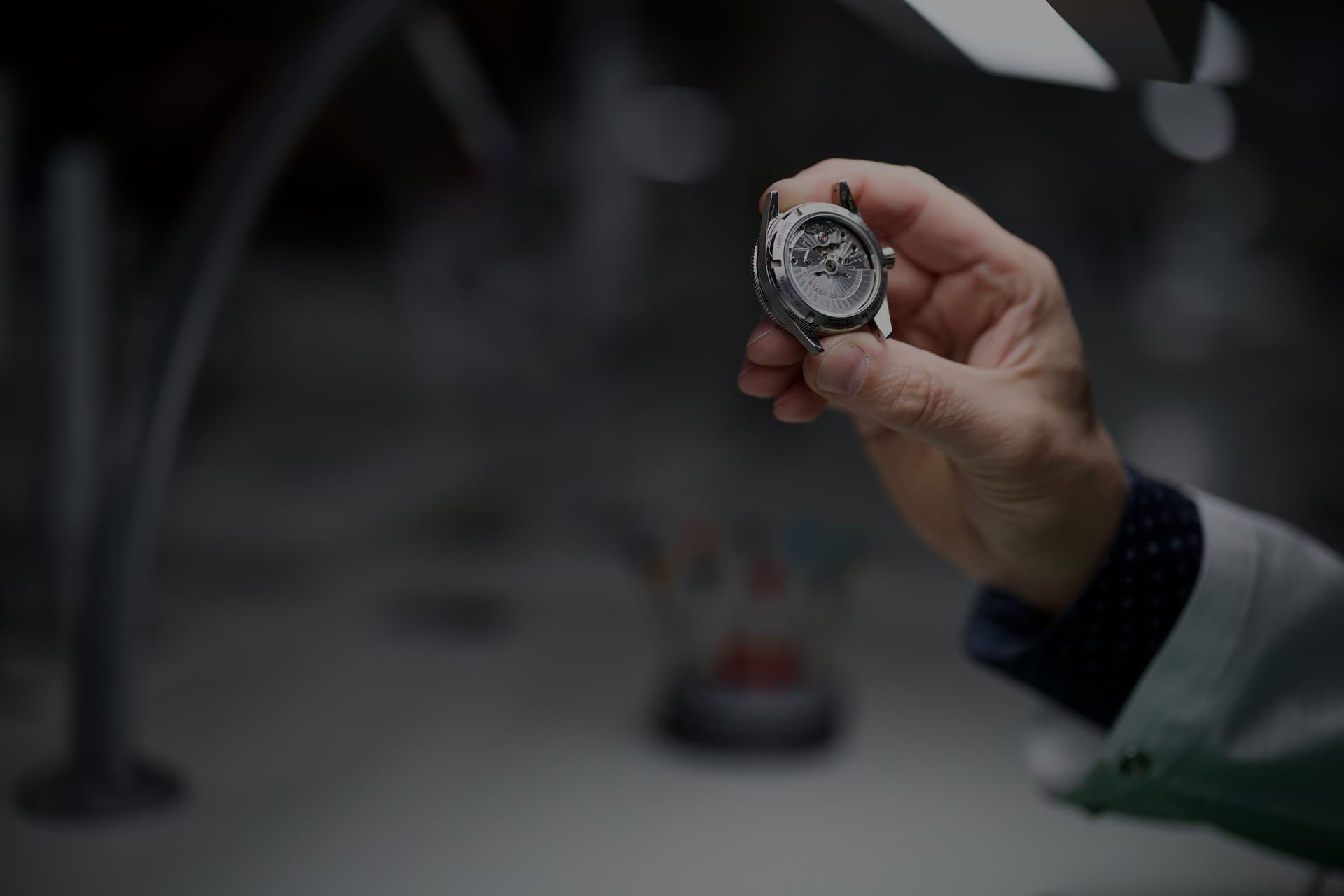 watchmaker's hand holding a watch facing the caseback under low light