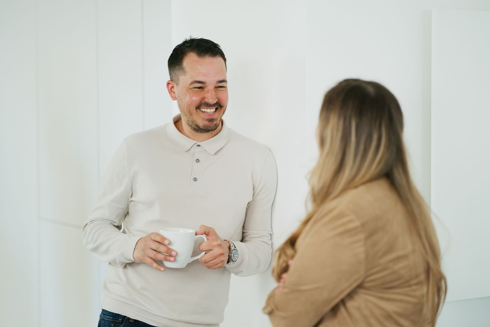 Ein Mann und eine Frau stehen in einem hellen Büroraum und unterhalten sich. Der Mann hält eine Kaffeetasse in der Hand, beide wirken in das Gespräch vertieft.