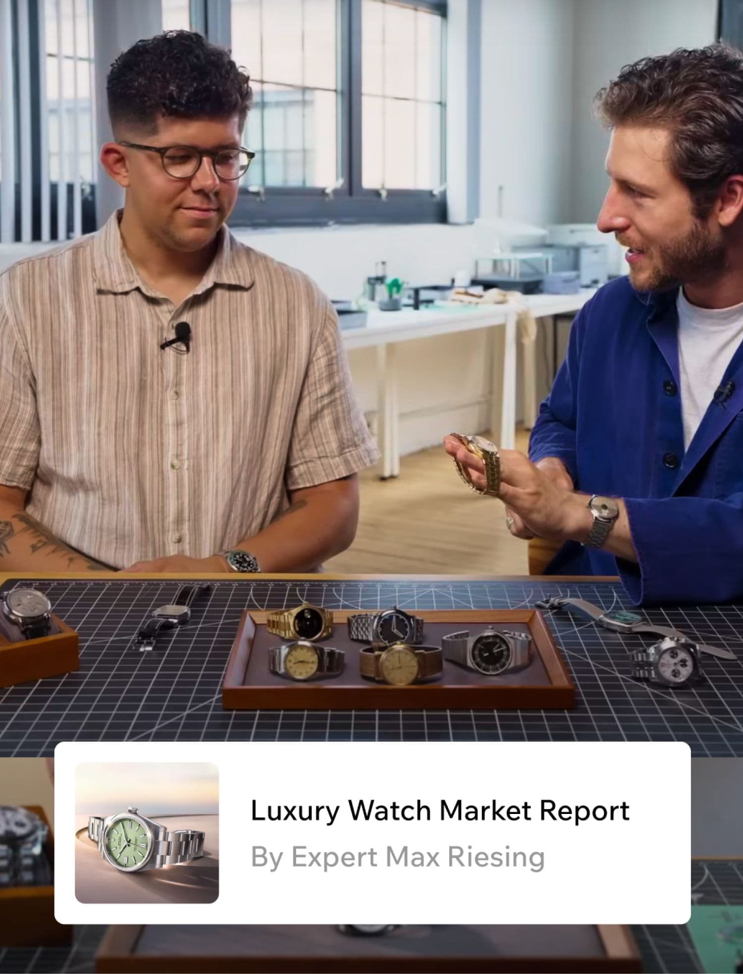 Two people discussing watches at a table with several luxury watches displayed, in a bright room.